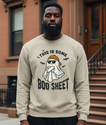 Man wearing a beige sweatshirt with a ghost and text design, standing in front of a brown building.