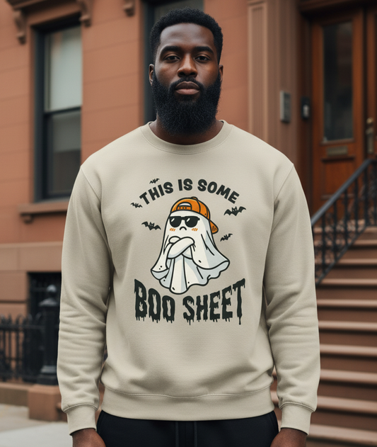Man wearing a beige sweatshirt with a ghost and text design, standing in front of a brown building.